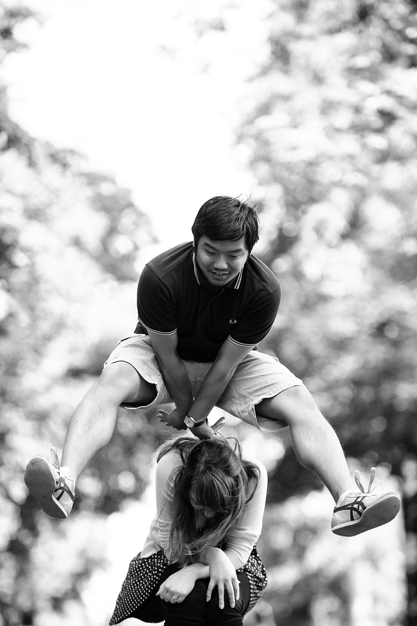 Playful couple having fun outdoors with joyful jumping movements in black and white.