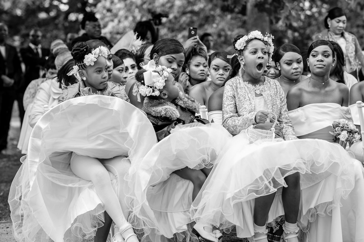 Large group of wedding guests in white outfits posed together outdoors.