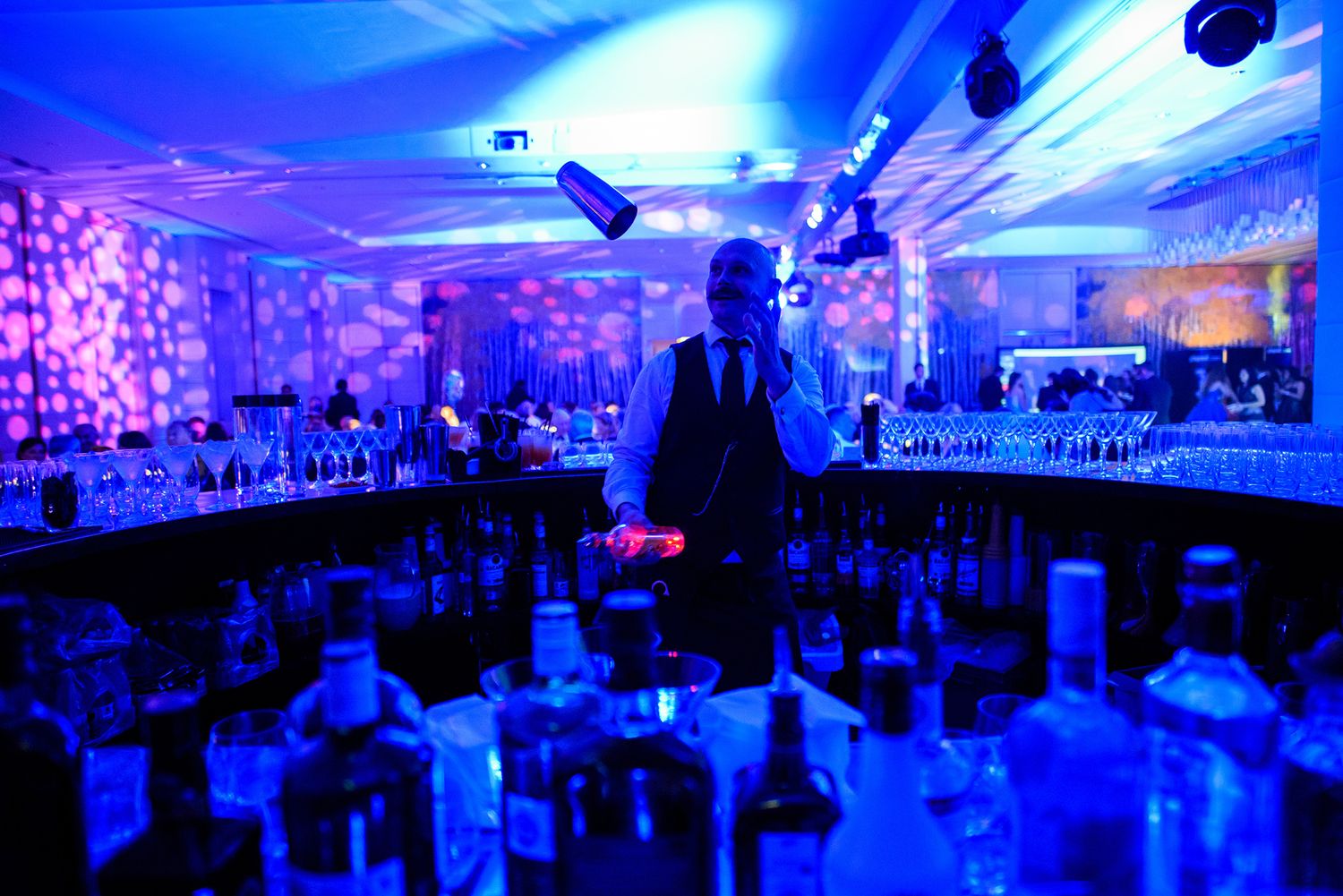 Dramatic blue lighting illuminates a crowded event space filled with party guests on the dance floor.