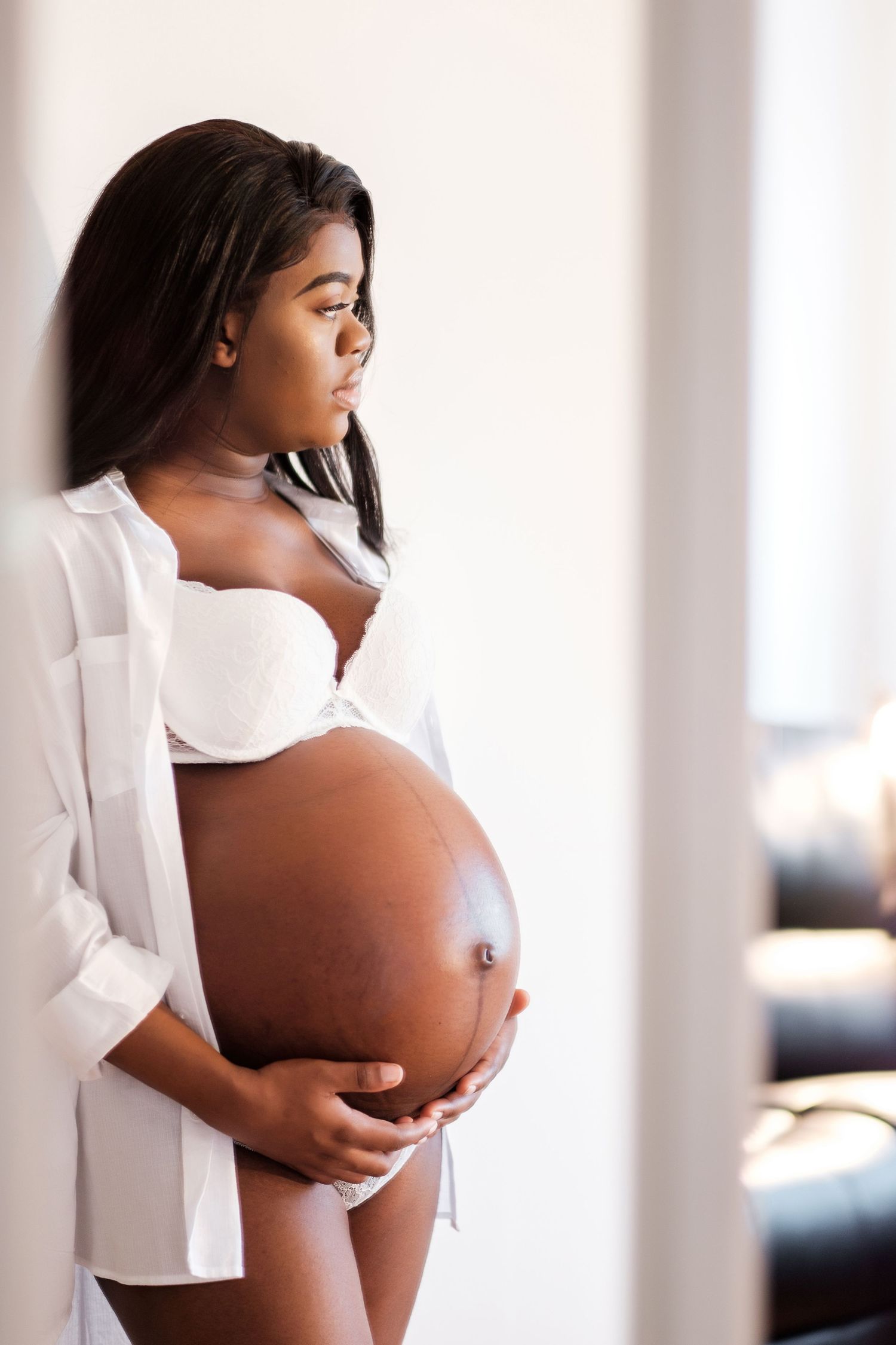 Artistic maternity photo showing an expectant mother in white against bright interior setting.