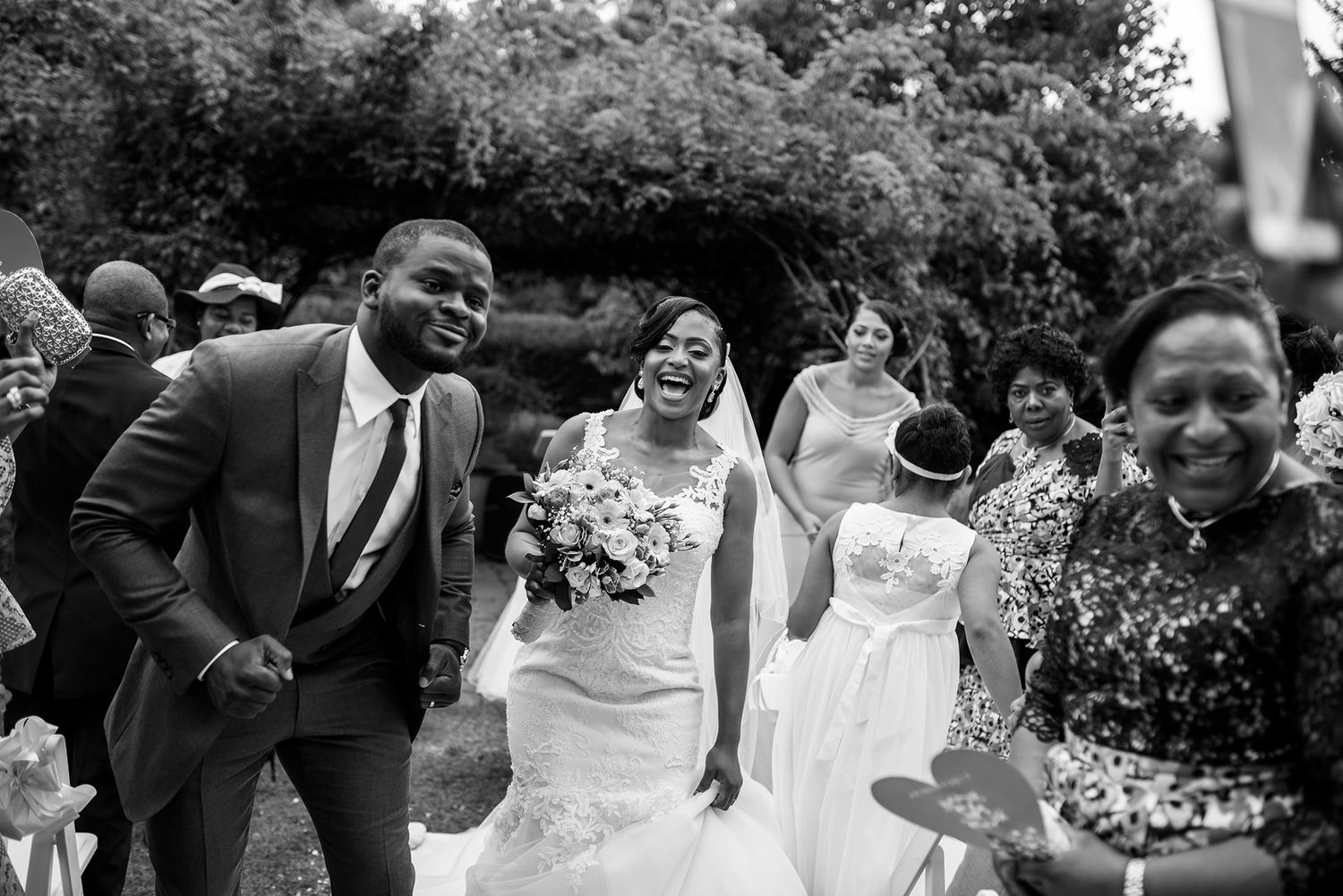 Wedding party and guests celebrating with animated expressions in an outdoor setting.