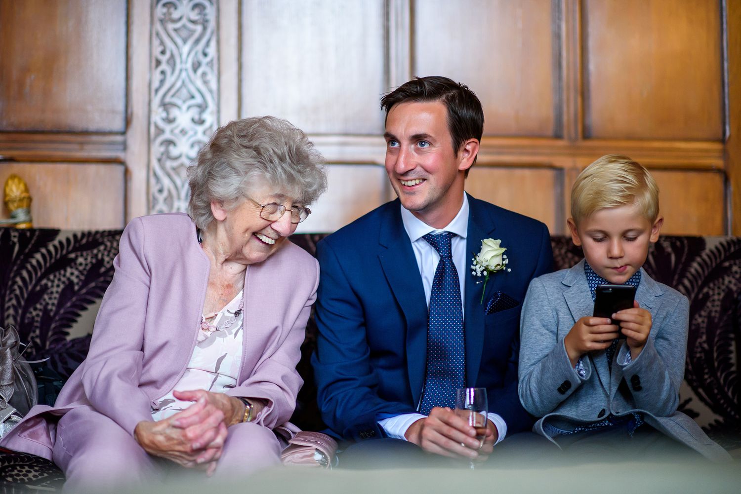 Three generations share a lighthearted moment on an ornate wooden bench.