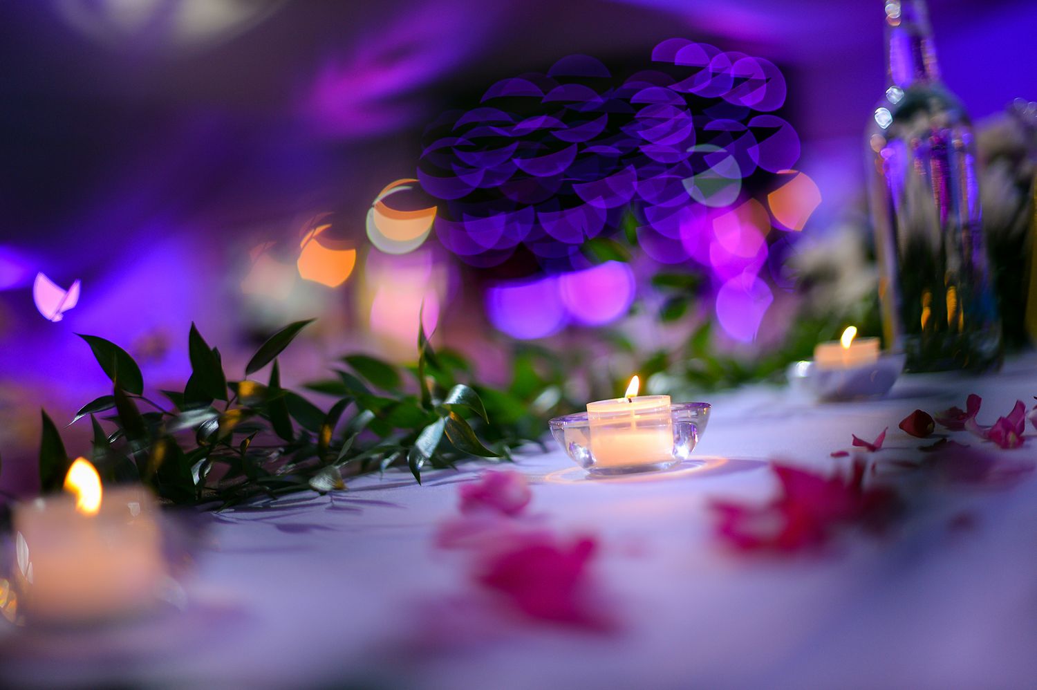Romantic table setting with glowing candles and purple bokeh lighting effects.