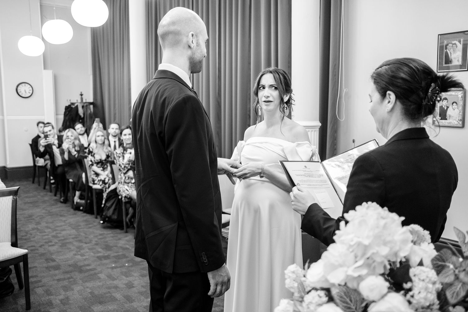 Wedding guests celebrate during an indoor ceremony with joyful expressions and formal attire.