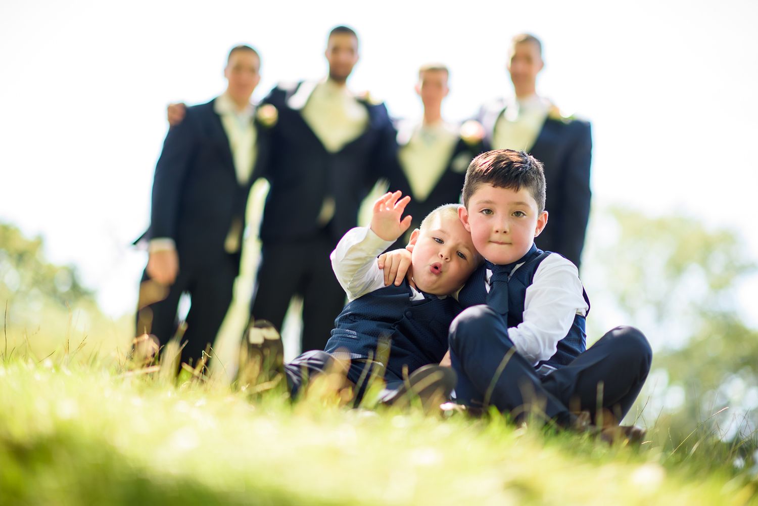 Two children playing on grass while formally dressed adults stand in the background.