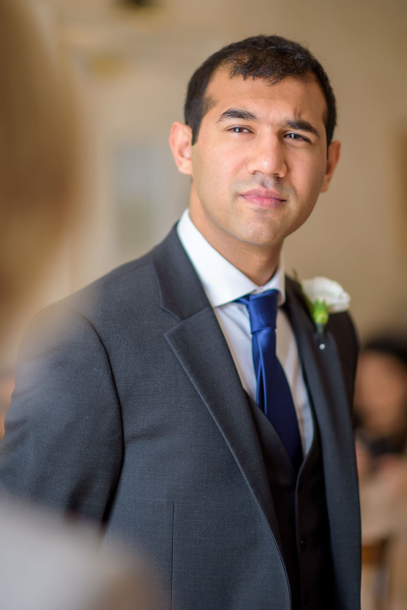 Close-up portrait series of a groomsman in a charcoal suit and navy tie at a formal wedding event.