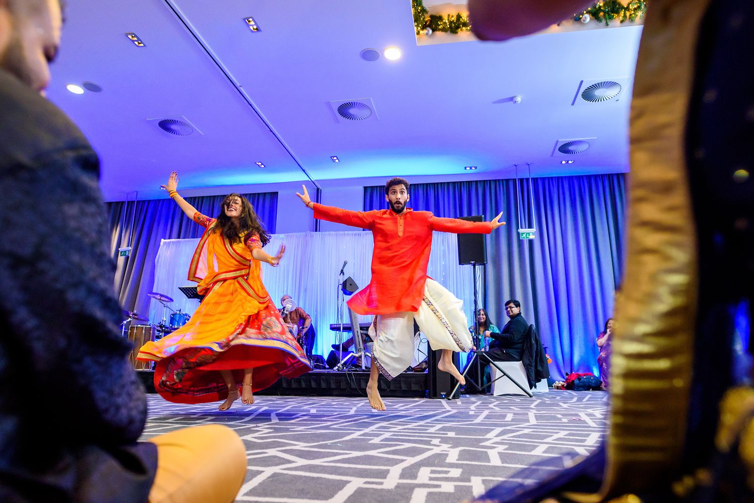 Energetic dancers in bright traditional attire perform choreographed moves on a blue-lit dance floor.