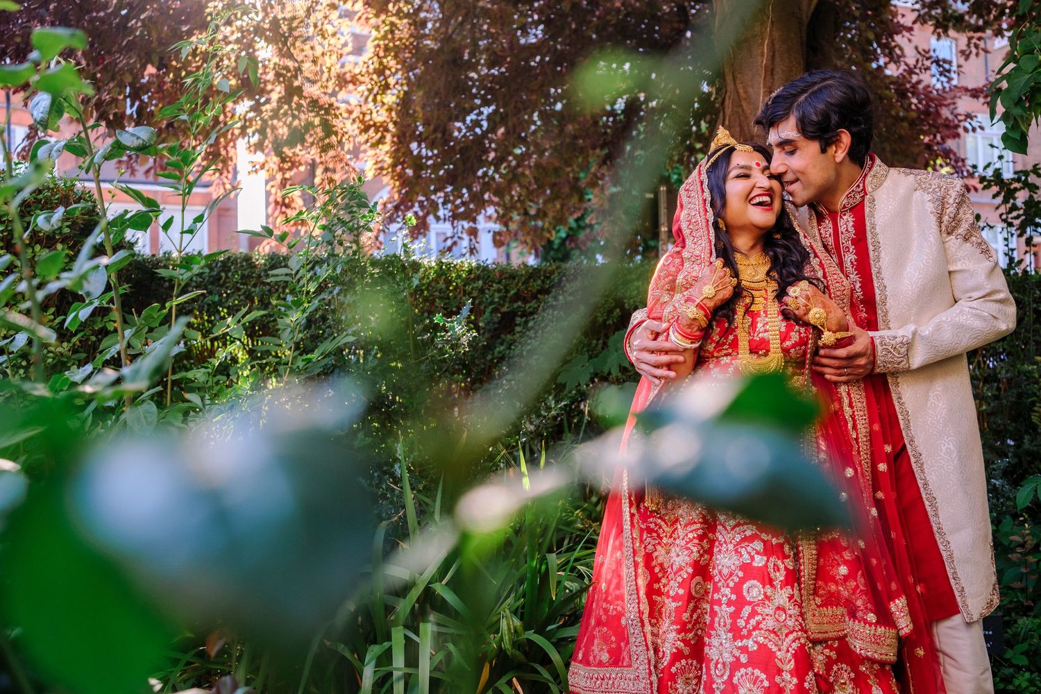 Romantic outdoor wedding portrait of couple in traditional Indian attire among blooming flowers.