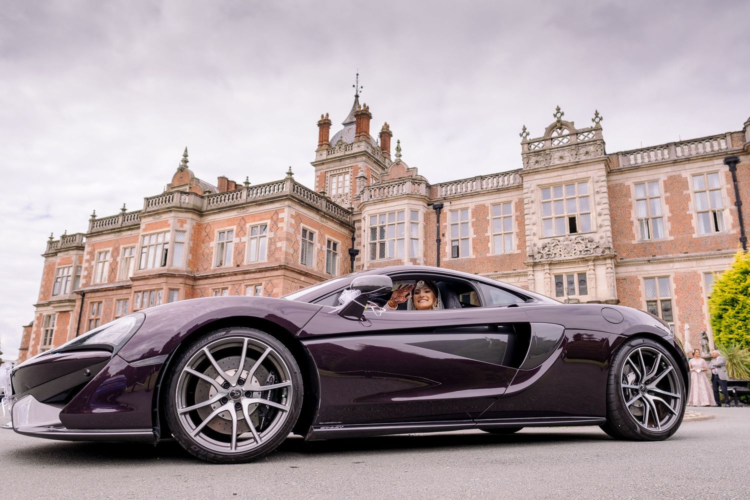 Purple McLaren supercar parked in front of a grand historic mansion.