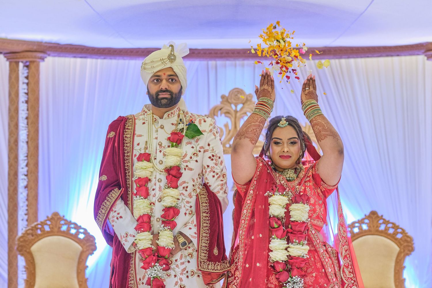 A couple performs a traditional Indian wedding ceremony ritual under decorative white drapes and lighting.