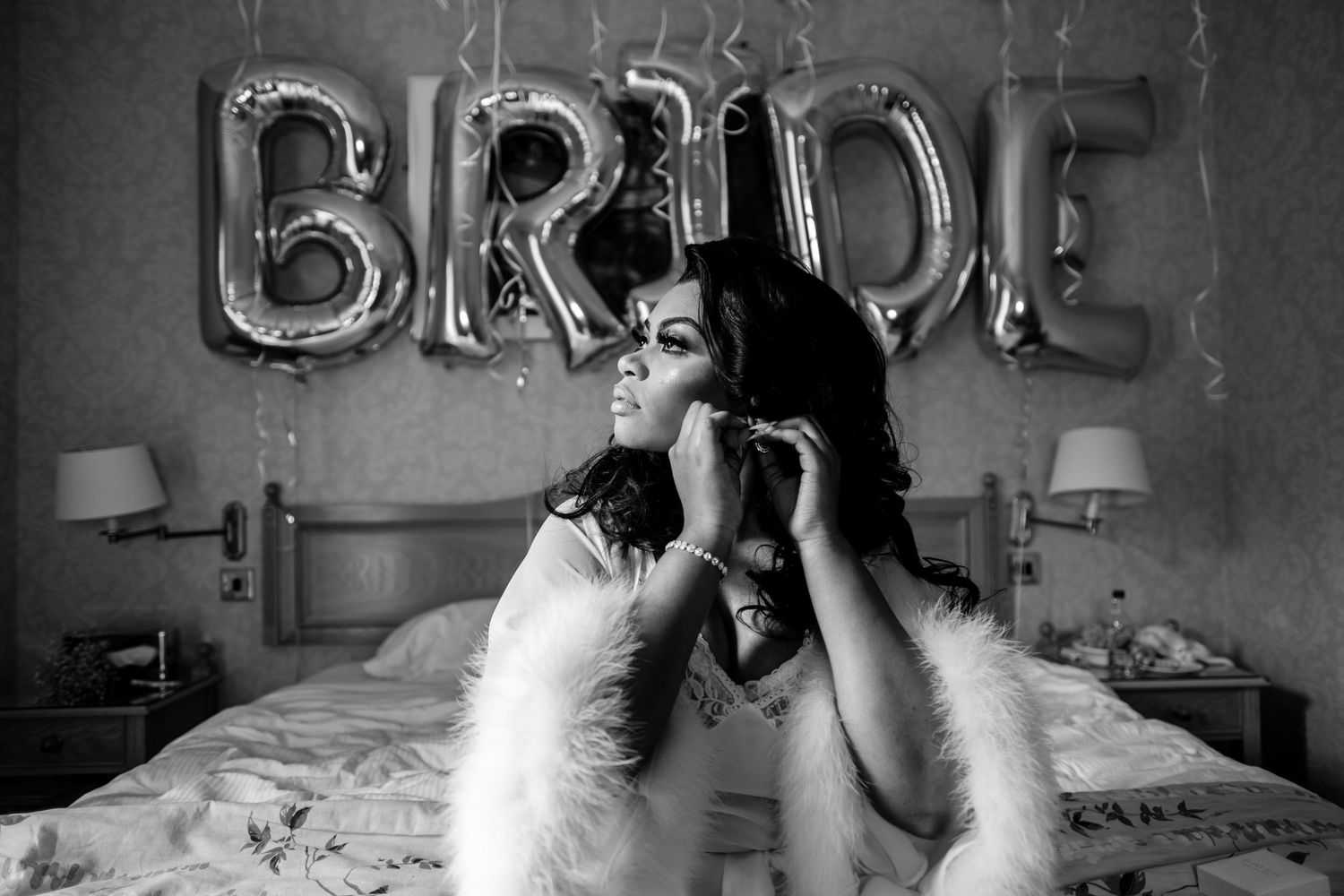 Black and white portrait with silver BRIDE balloons in background during wedding preparations.