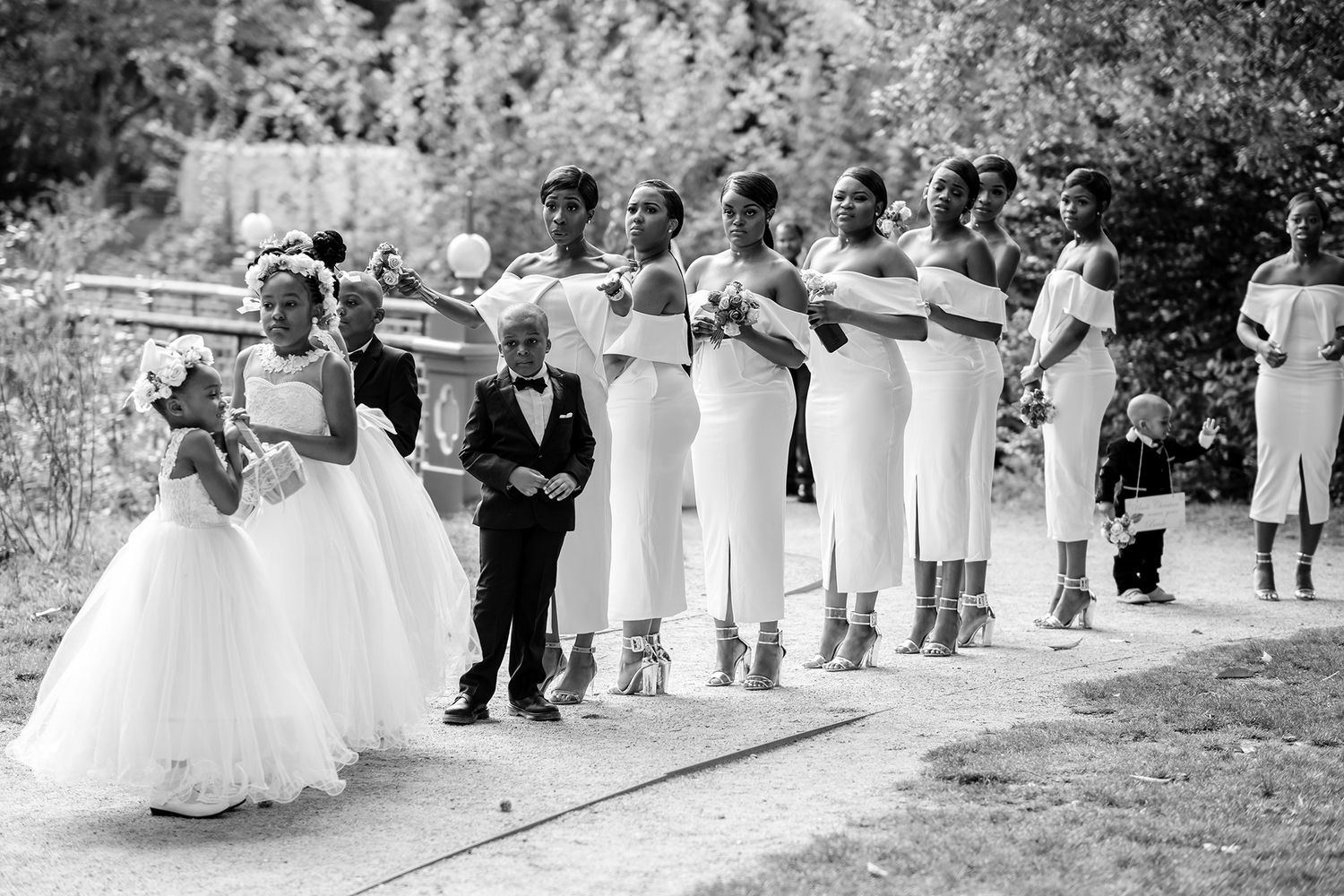 Wedding party members walking in formal attire through a garden setting.