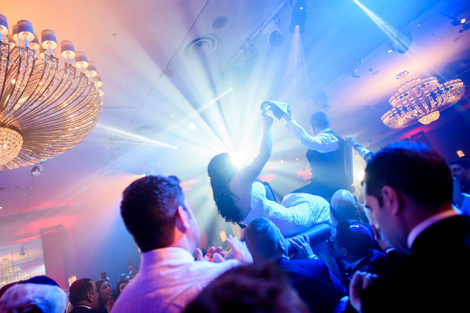 Dynamic party scene with bright spotlights and chandelier creating atmospheric lighting effects.