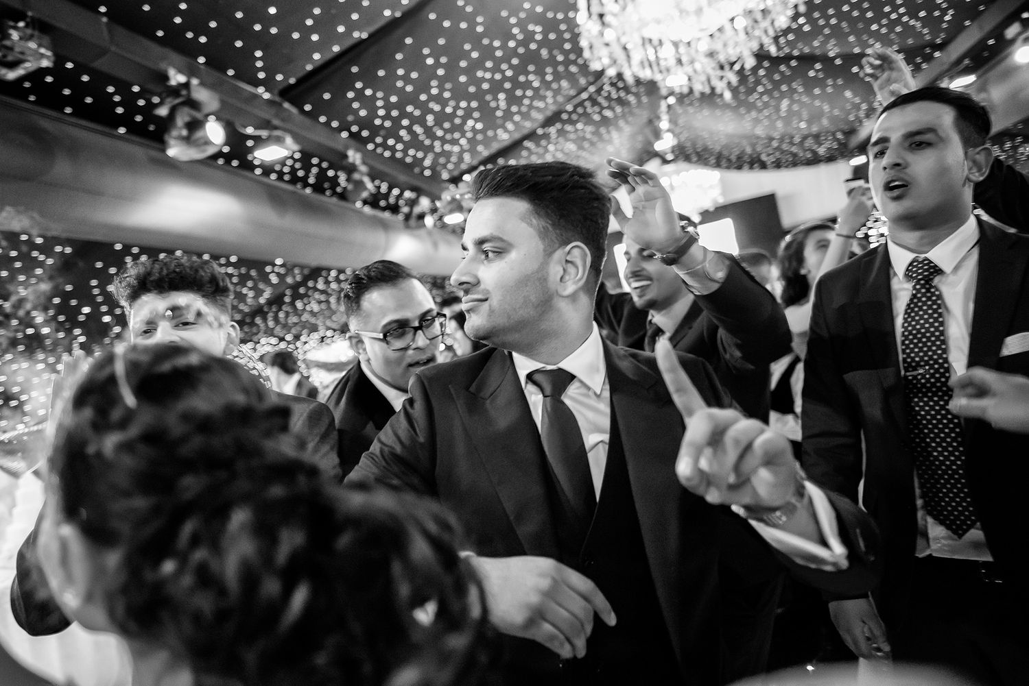 Wedding guests enjoying themselves on a festive dance floor under a sparkling chandelier.