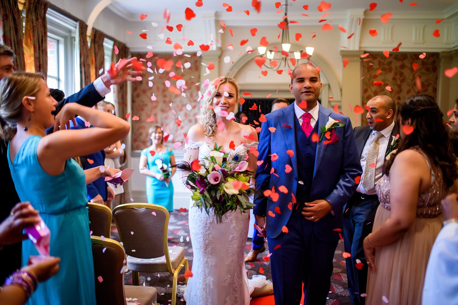 Red heart confetti floats through the air during a joyous wedding celebration.