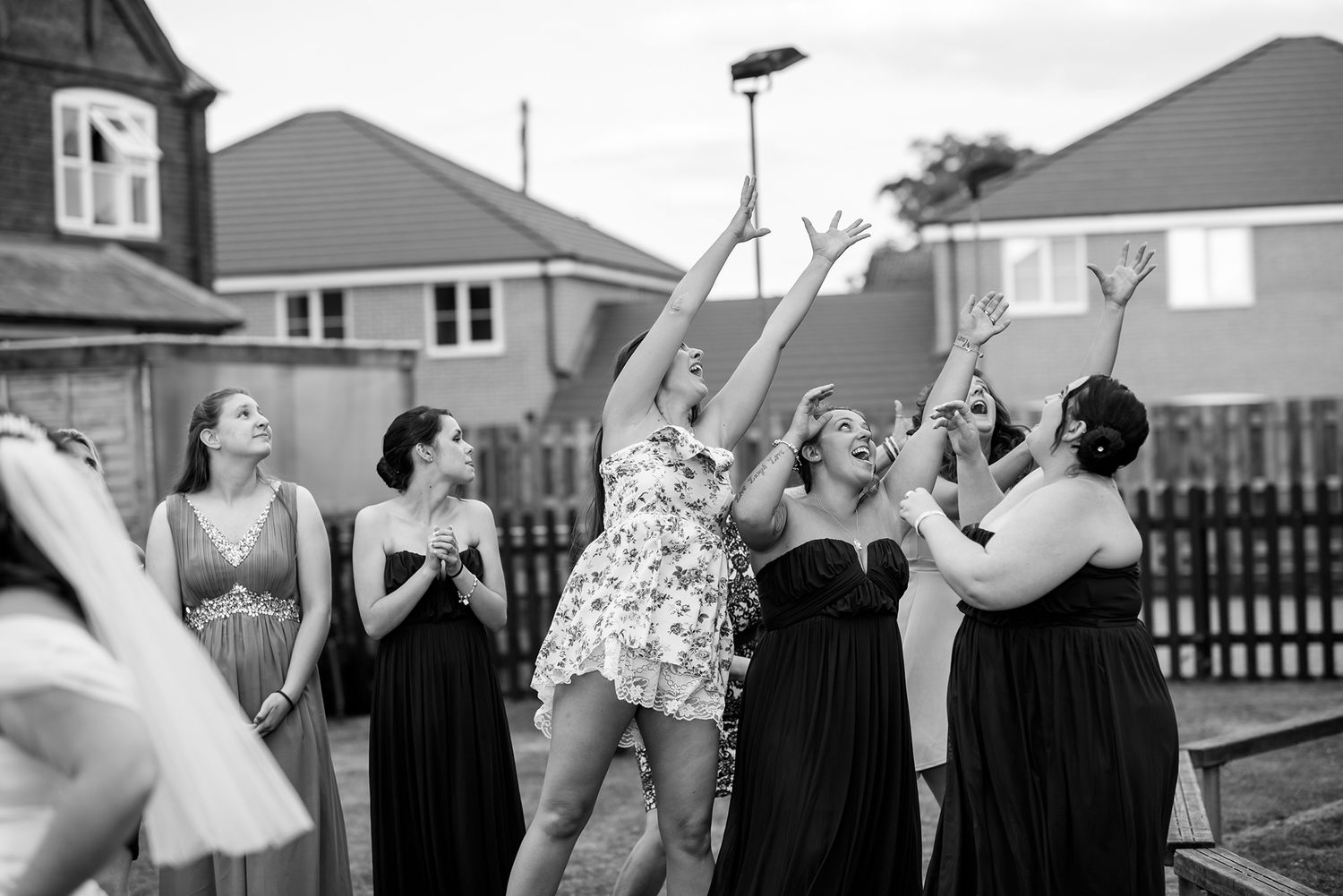 Wedding party poses candidly outside suburban homes in black and white photography.