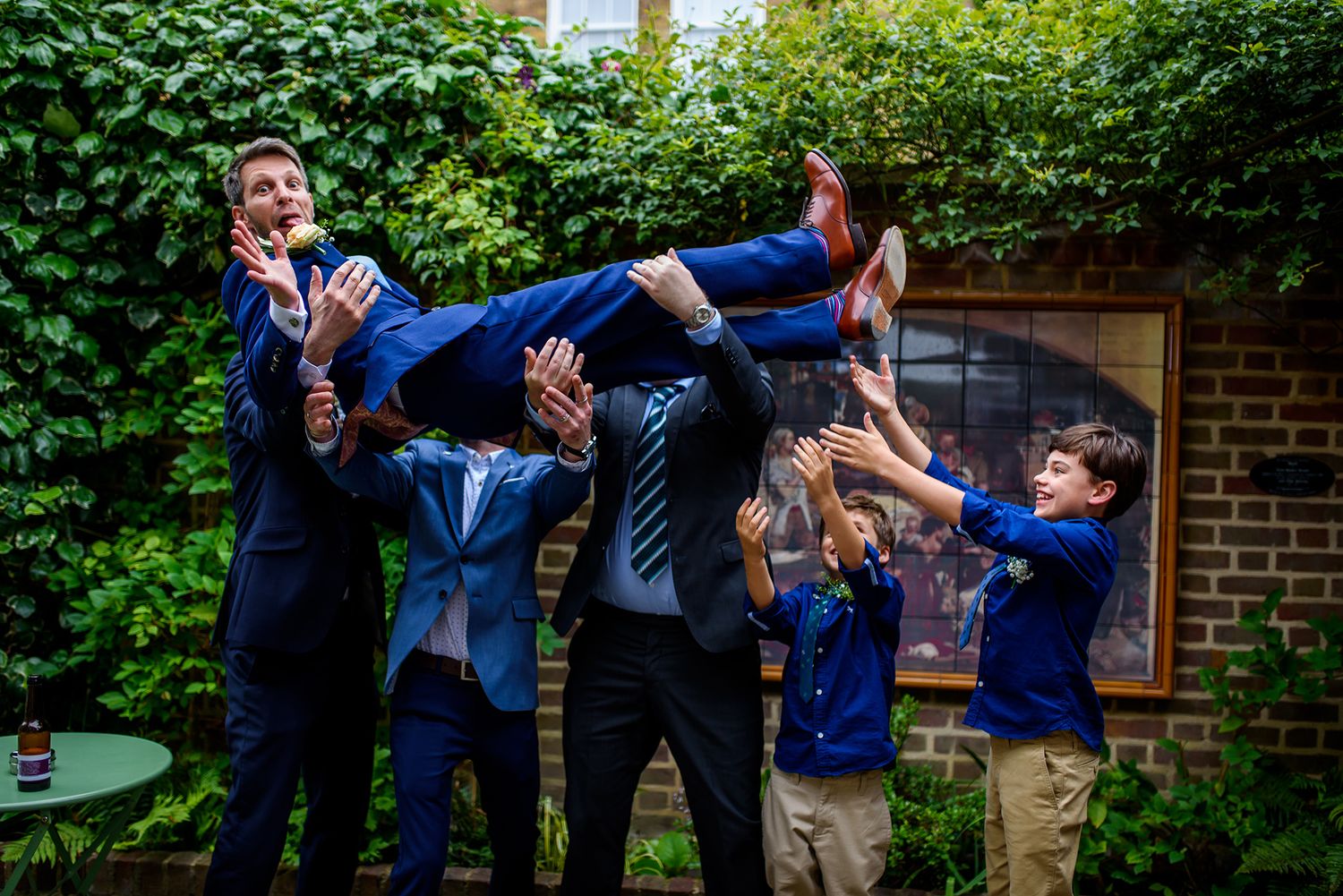 Wedding party members holding someone up high in a playful outdoor group pose.