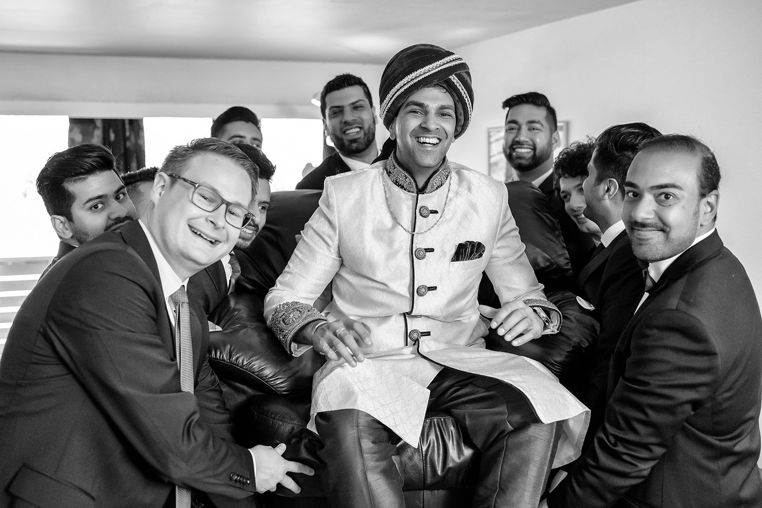 A celebratory group photo showing groomsmen lifting someone in traditional Indian wedding attire.
