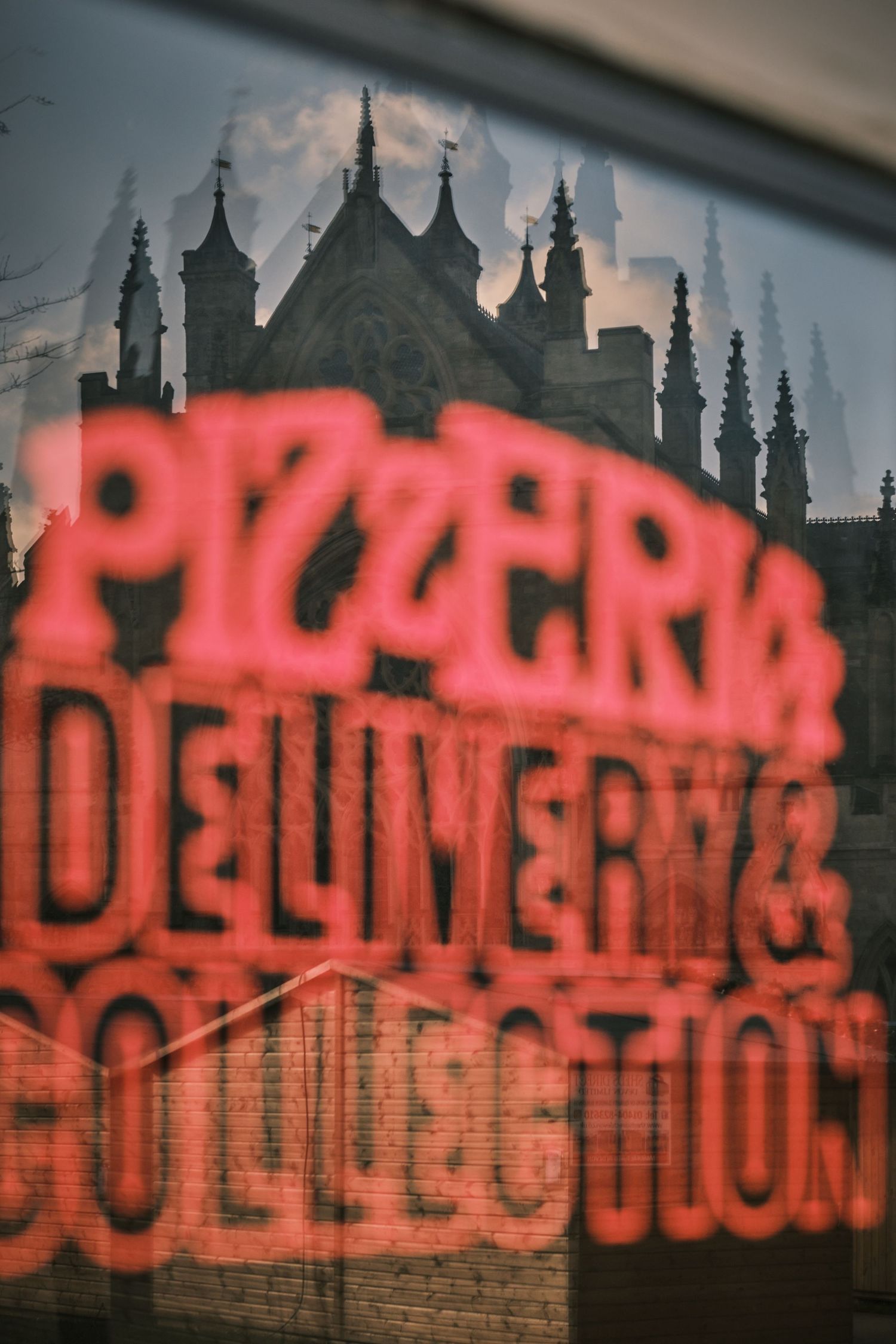 Red neon sign reflecting cityscape silhouettes against a window at twilight.