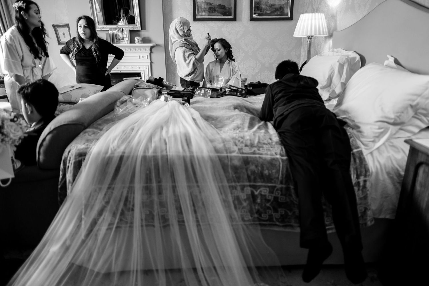 A black and white wedding photograph showing a flowing bridal veil being arranged on a bed during preparation.