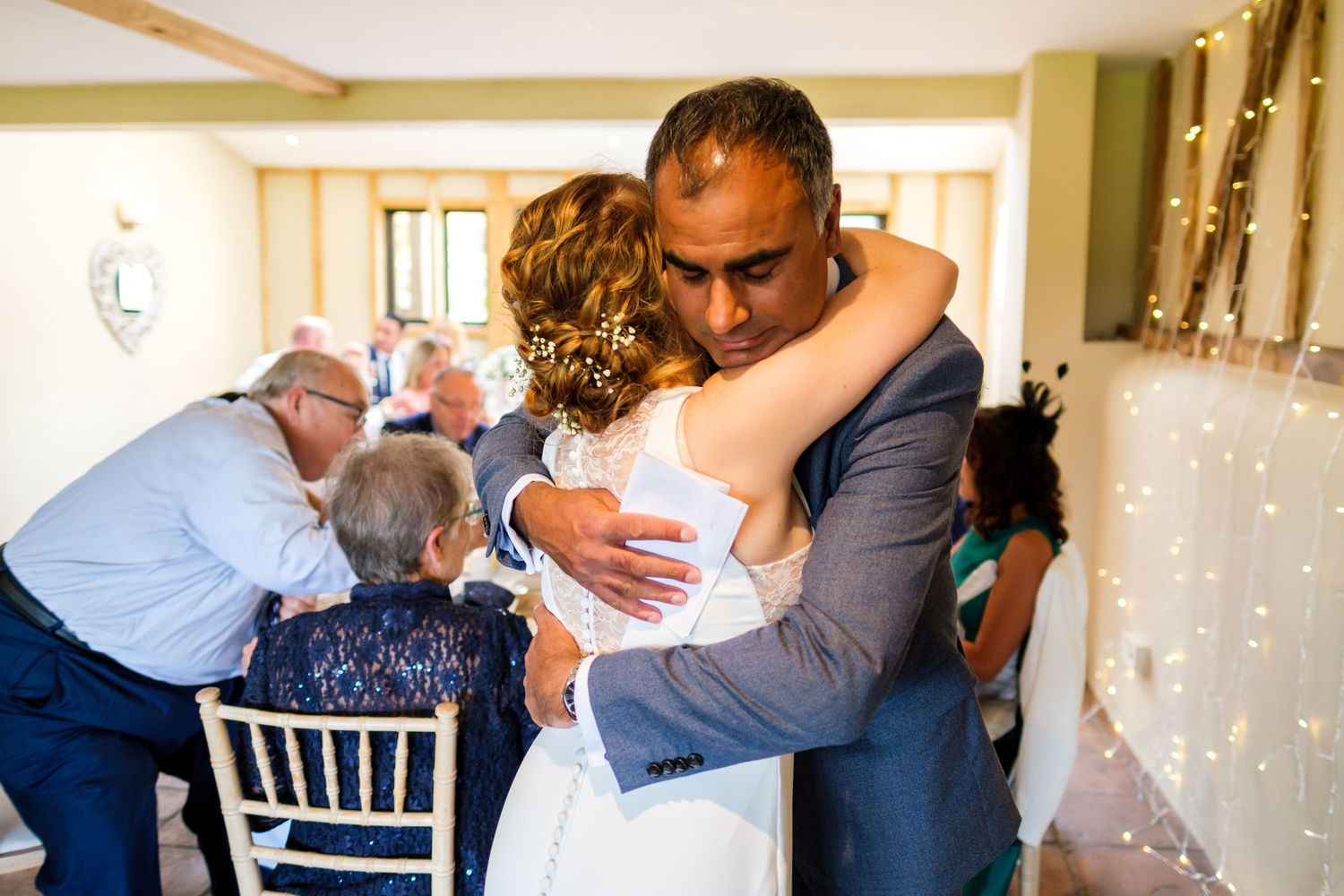 Wedding guests embracing and celebrating in a warmly lit venue with string lights.