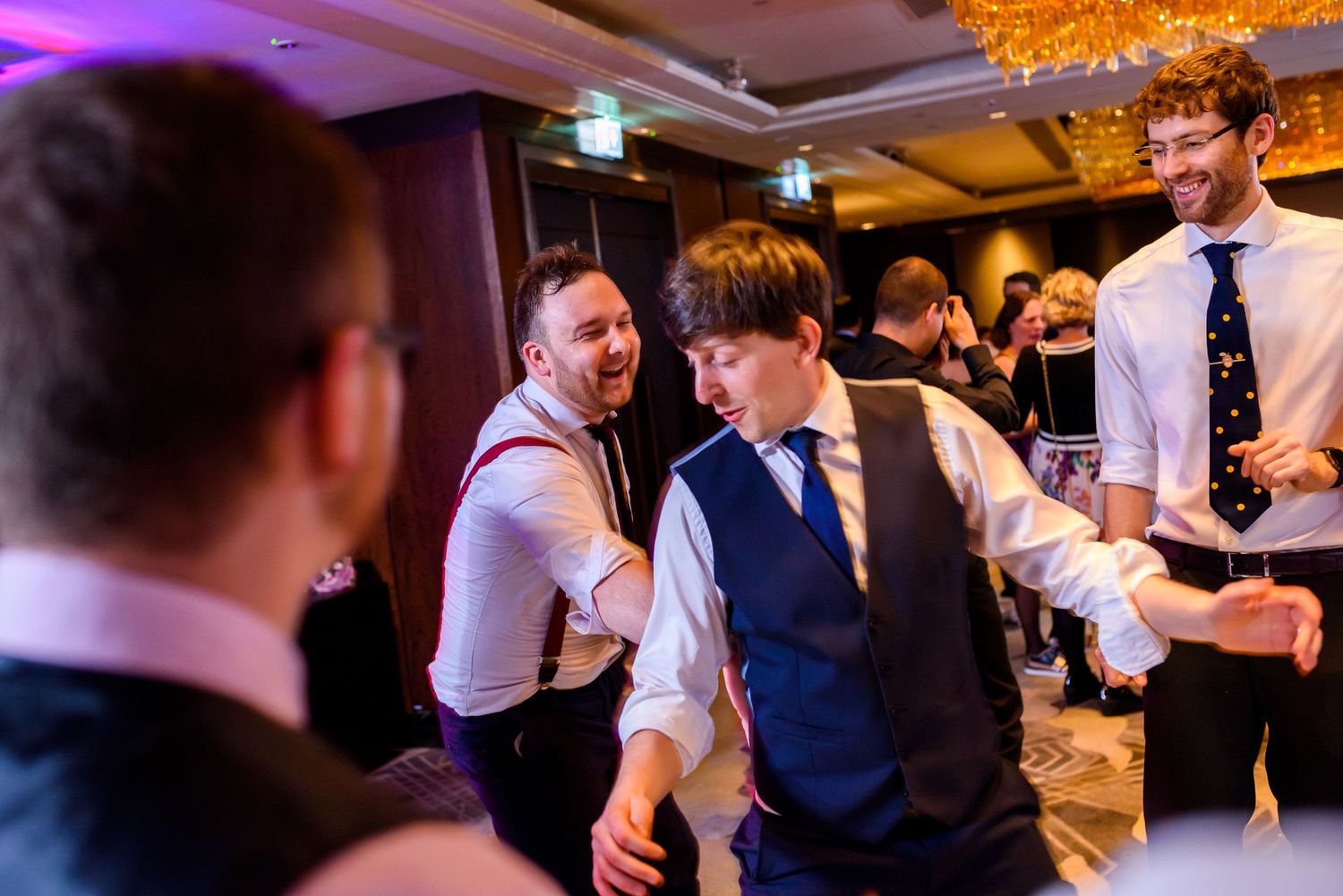 Guests dance and celebrate together at an elegant indoor wedding reception with warm lighting and festive atmosphere.