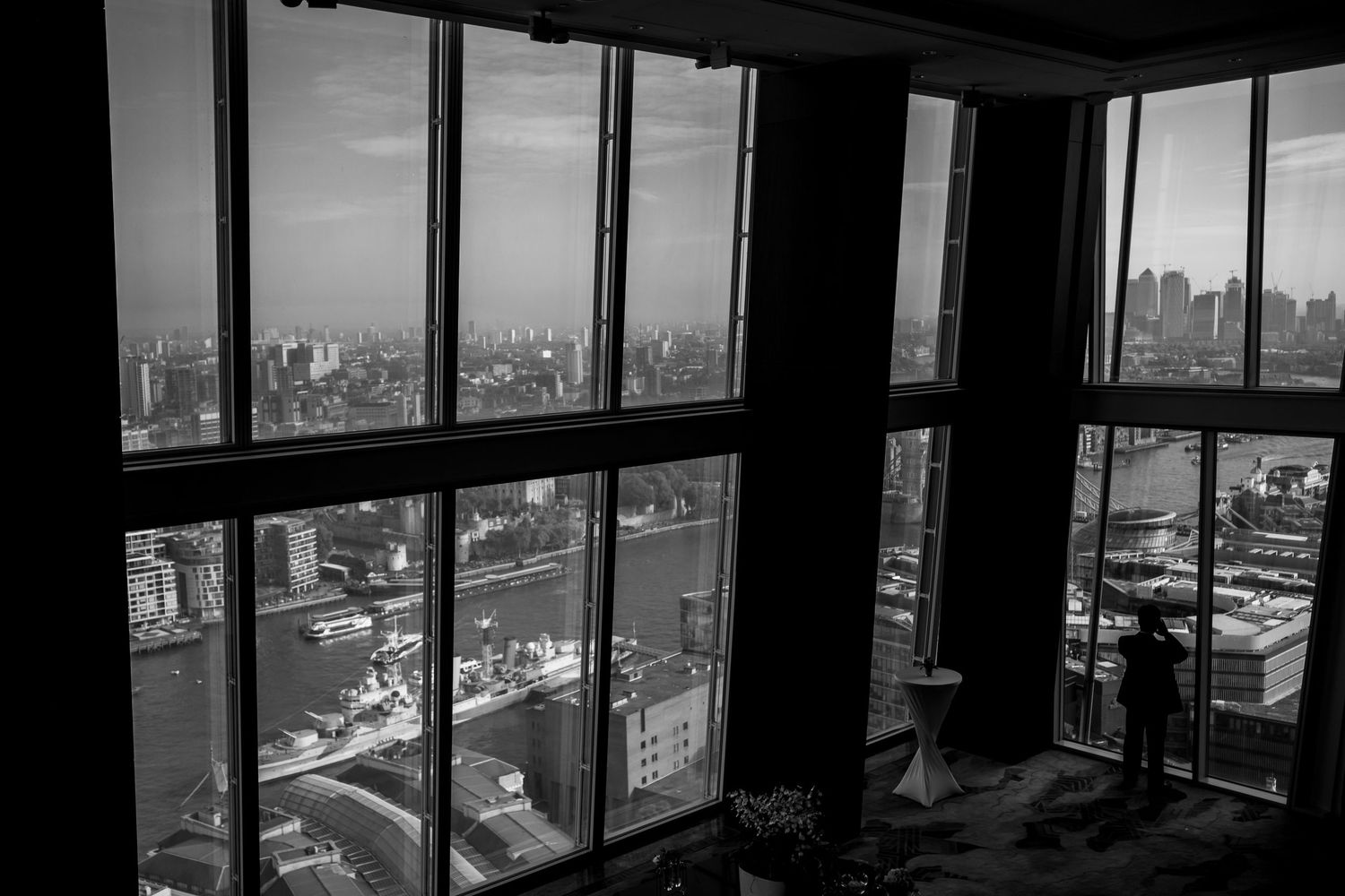 Black and white cityscape view through large windows showing urban skyline and buildings in dramatic lighting.