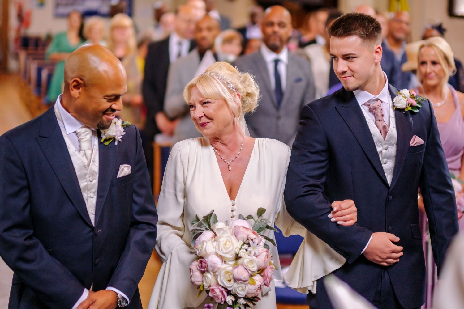 Wedding ceremony participants stand together with a beautiful pink and white floral bouquet in a church.