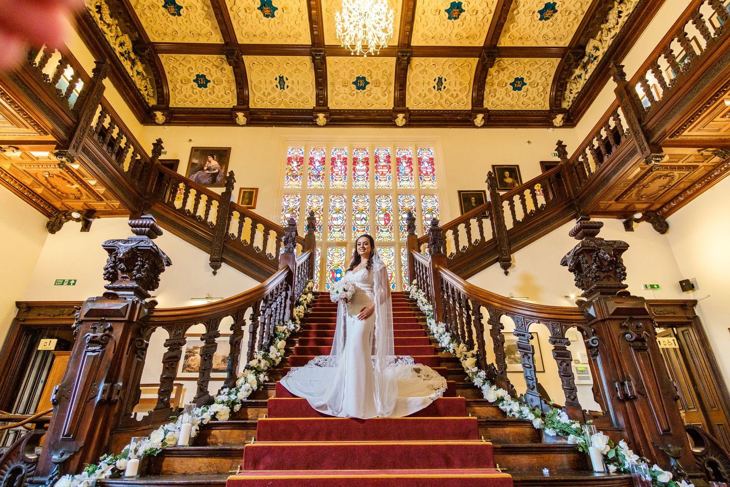 Elegant grand staircase in historic venue with ornate wooden details and chandelier lighting.