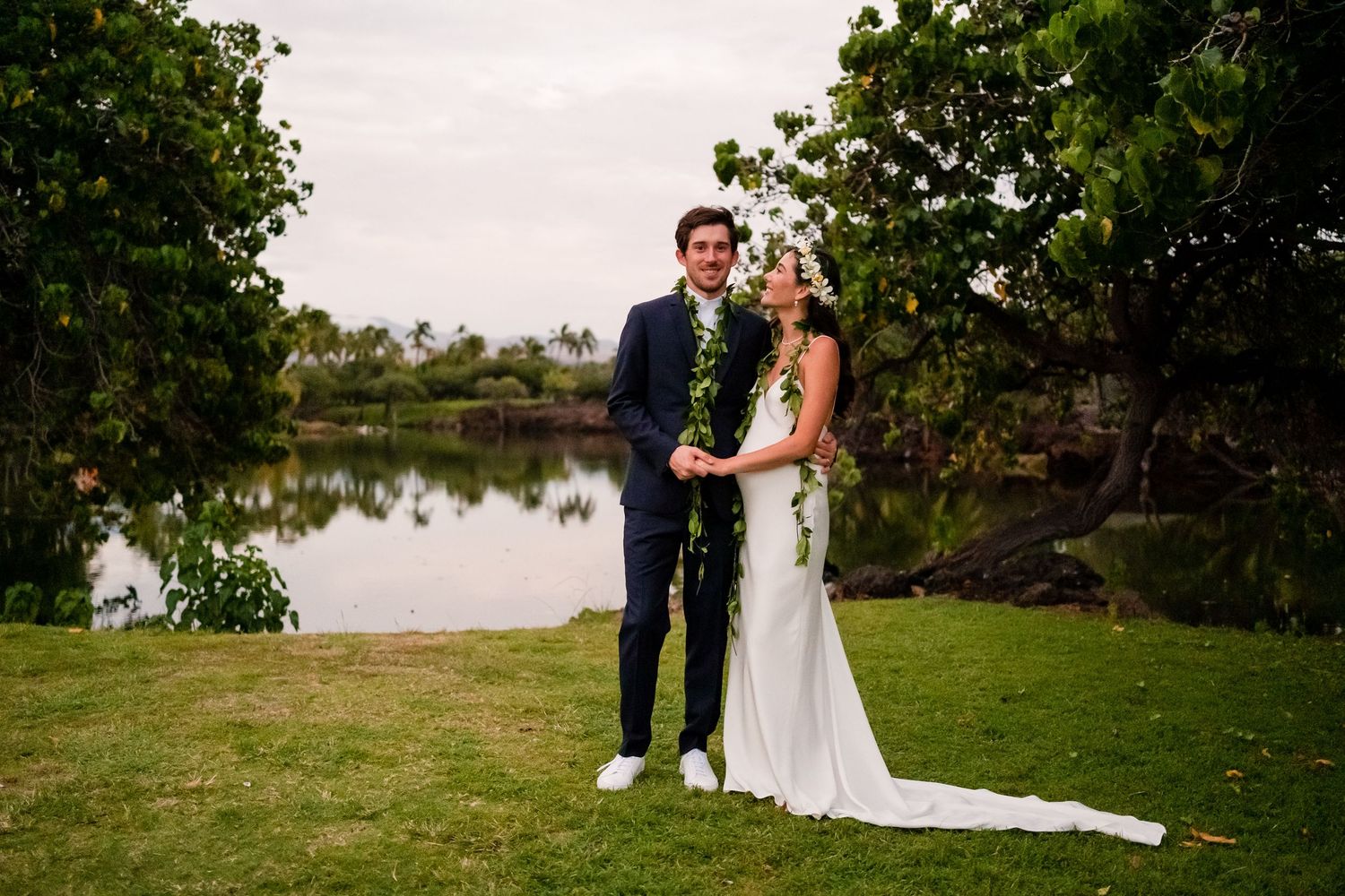 Romantic wedding portraits captured in a lush garden setting with palm trees and water views.