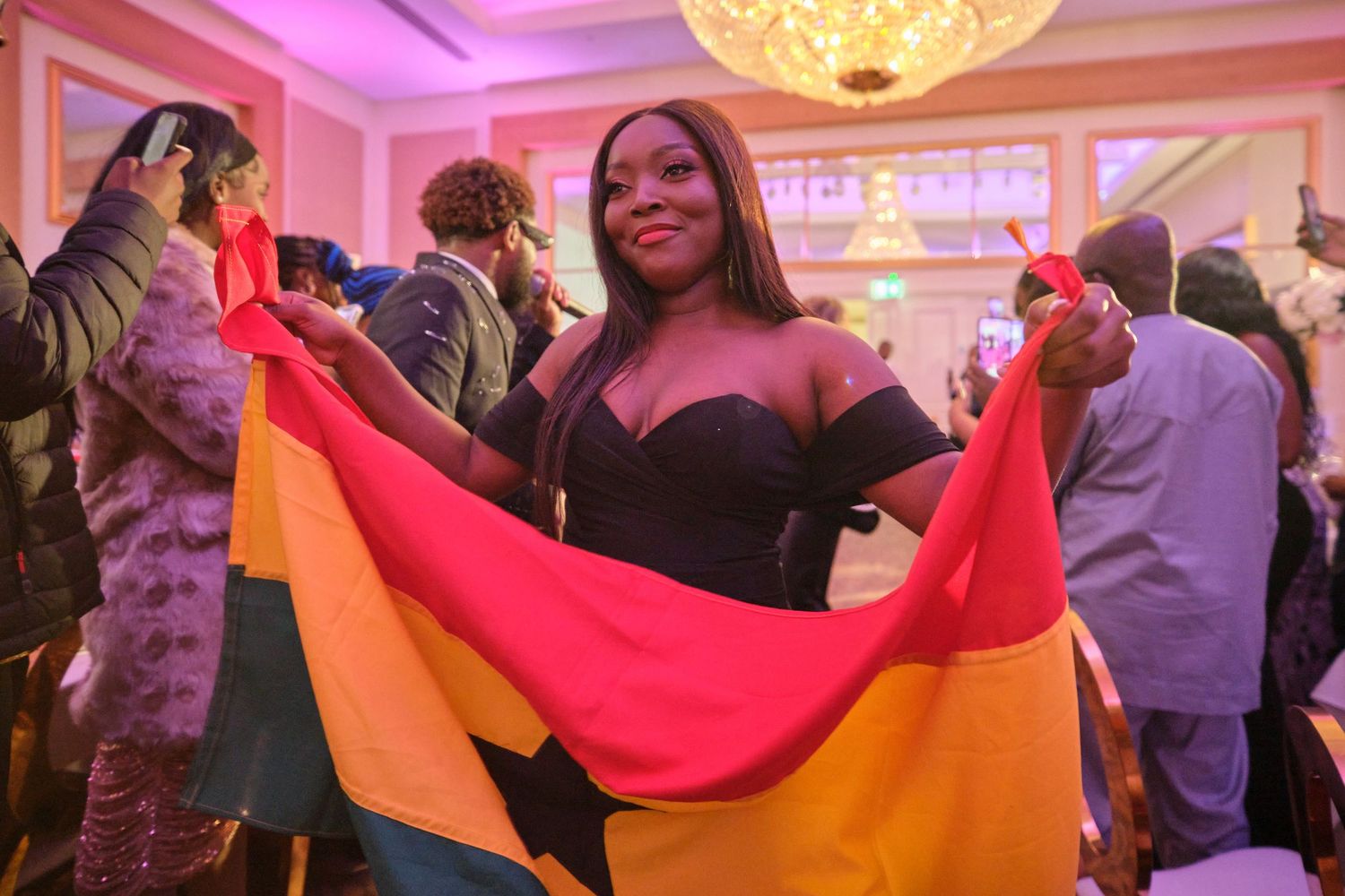 A person holds up a colorful red and orange flag while smiling in a warmly lit indoor venue during an event.