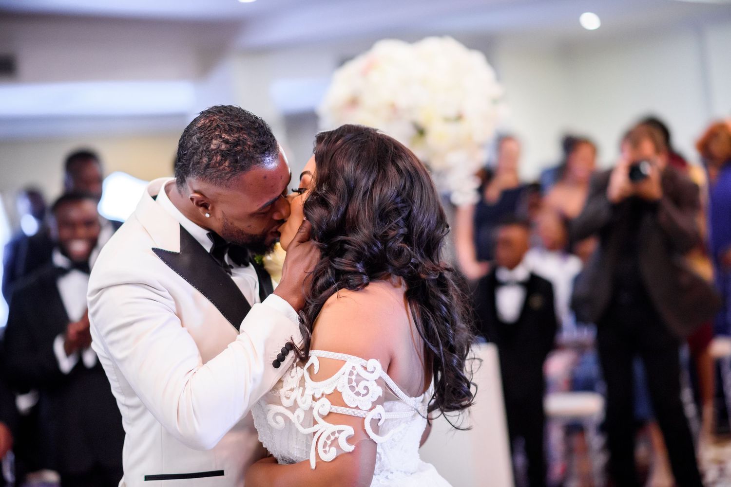 A wedding couple embraces on the dance floor surrounded by guests.
