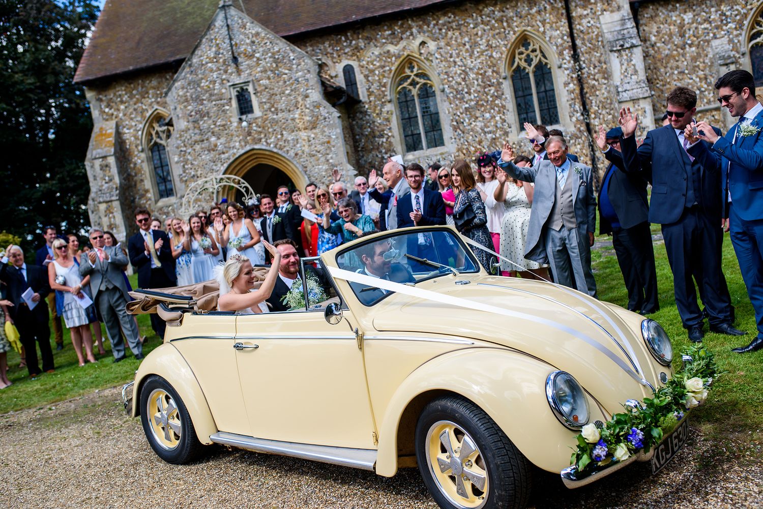 Classic cream colored vintage wedding cars parked outside a stone church.