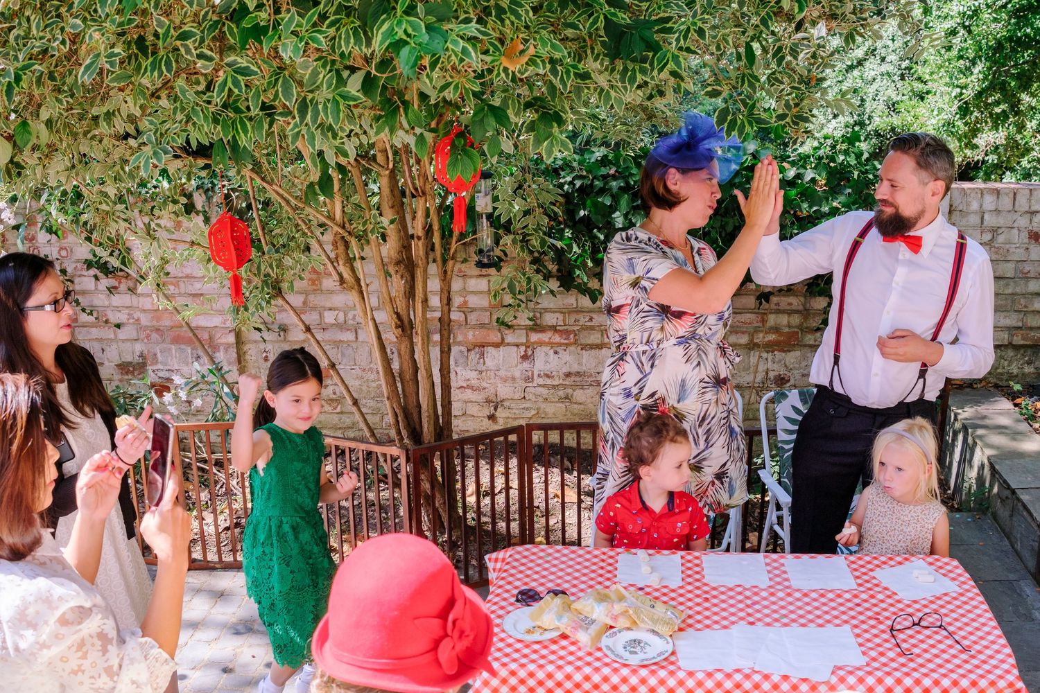 Couples dancing together at an outdoor garden party with red and white checkered tablecloths.