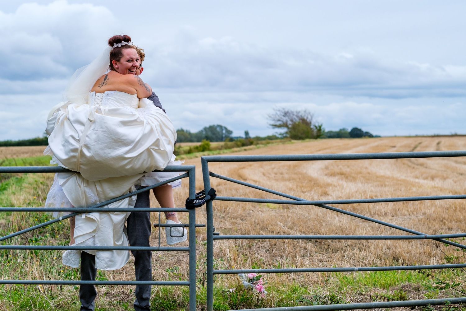 Wedding couple and party members pose along a rustic fence with countryside views.