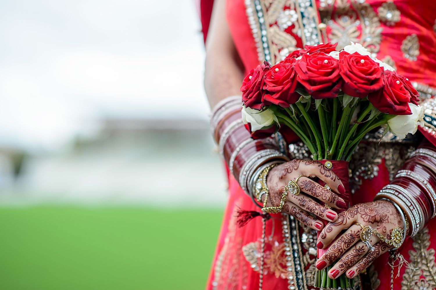 Close-up of hands holding vibrant red roses and traditional mehndi designs.
