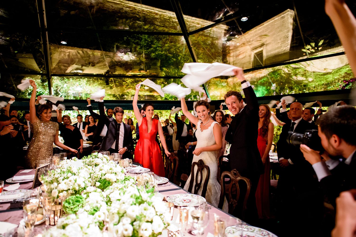 Reception tables decorated with lush floral arrangements under outdoor tent lighting.