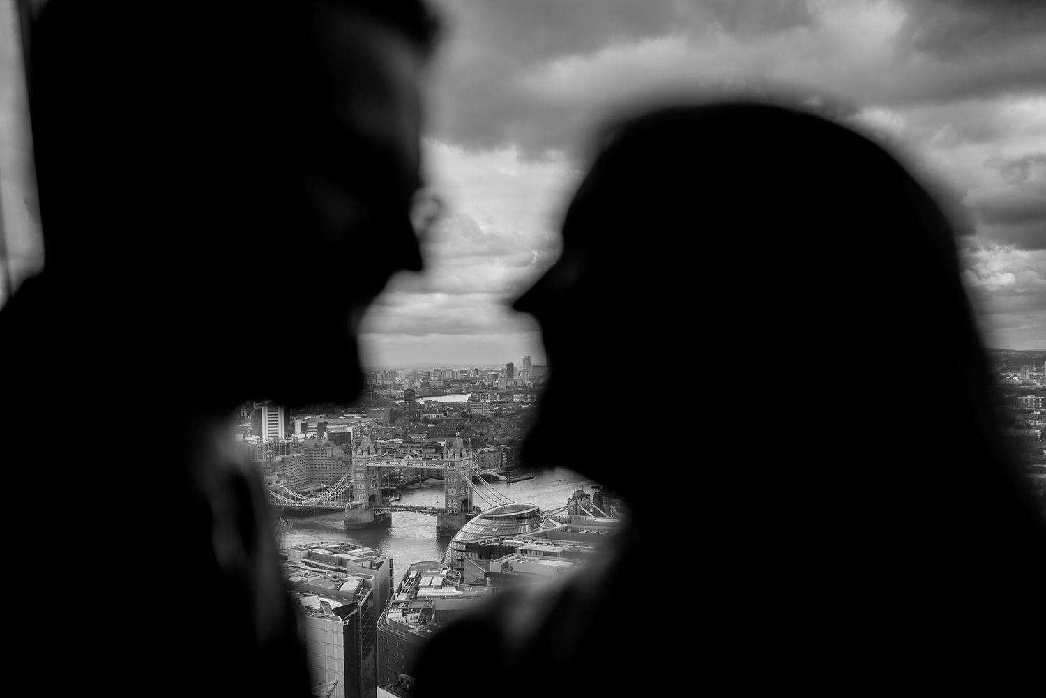 Dark silhouettes embrace while looking out over a dramatic urban skyline.