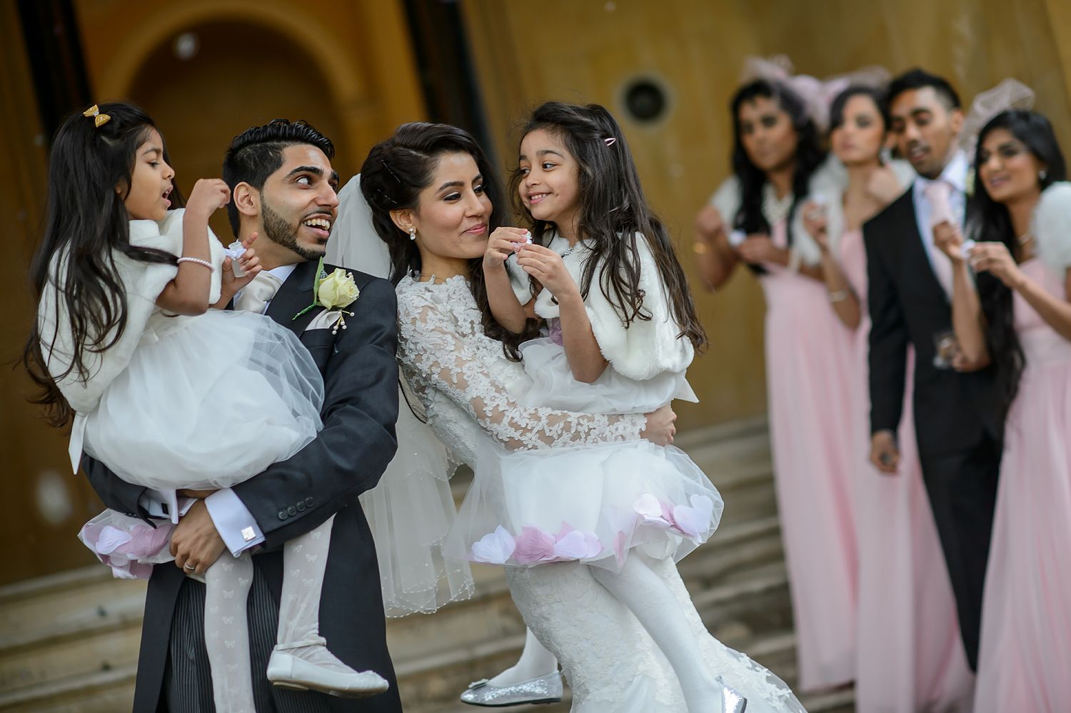 Wedding party shares joyful moment with children in formal attire outside venue.