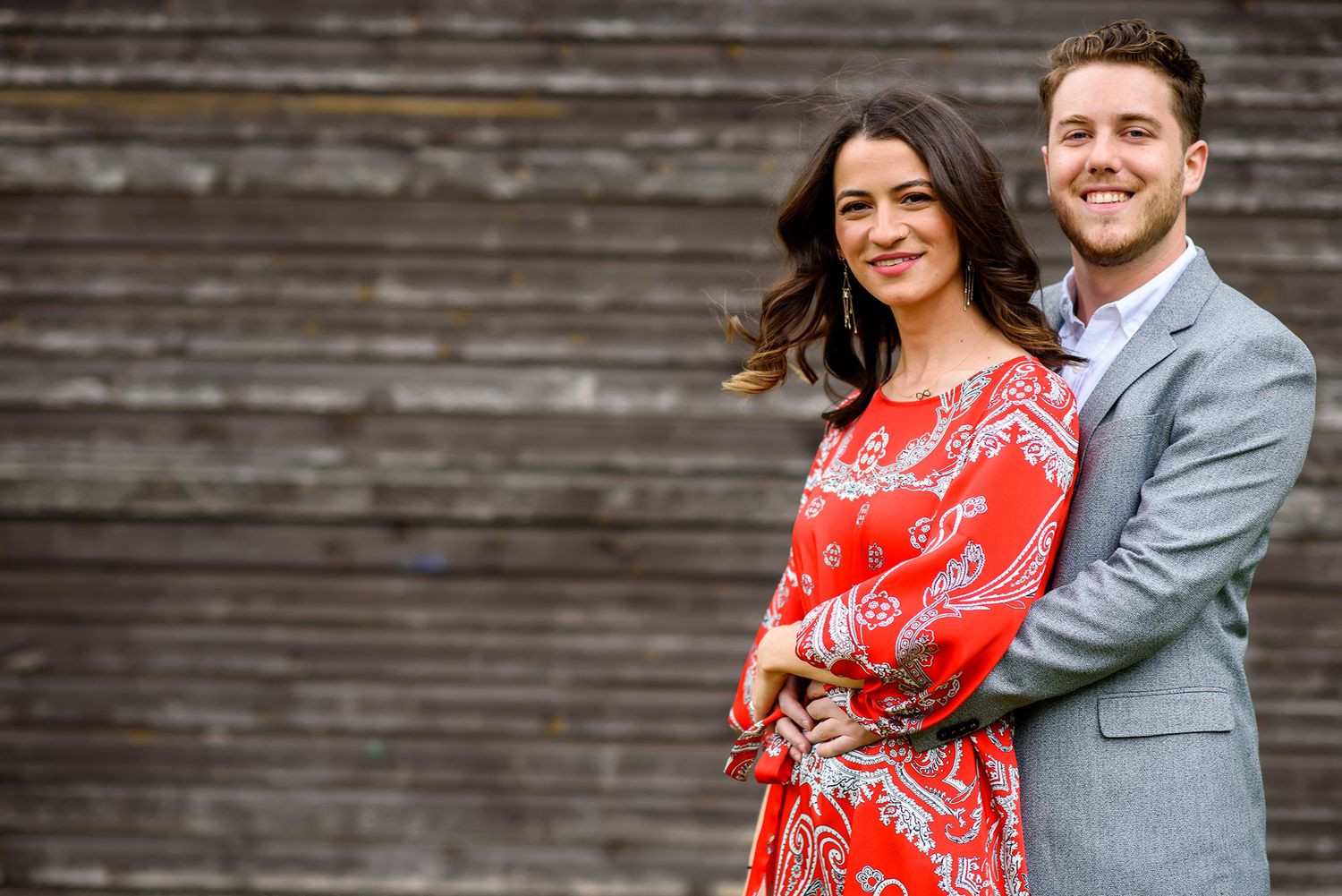 An engagement portrait of a couple in front of weathered wooden siding.