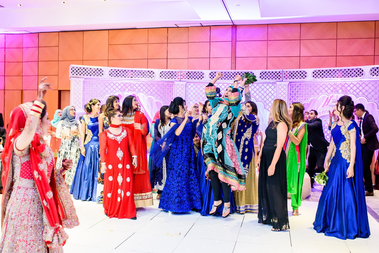 Panoramic view of wedding guests in colorful traditional attire against pink-lit backdrop.