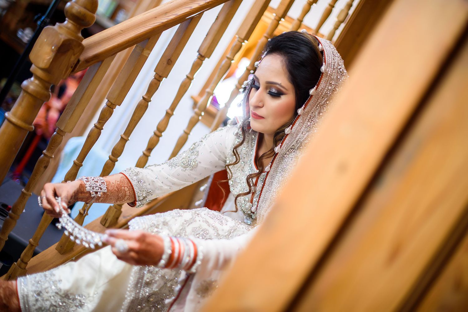 A delicate lace veil adorns a traditional bride seated on stairs during wedding preparations.