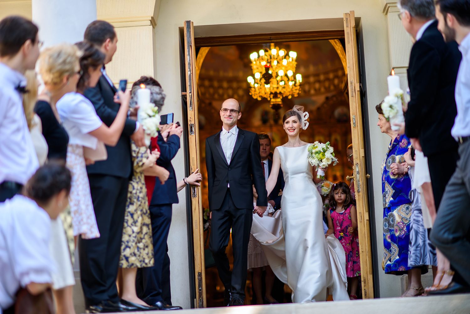 Wedding party and guests exiting ornate church building after ceremony.