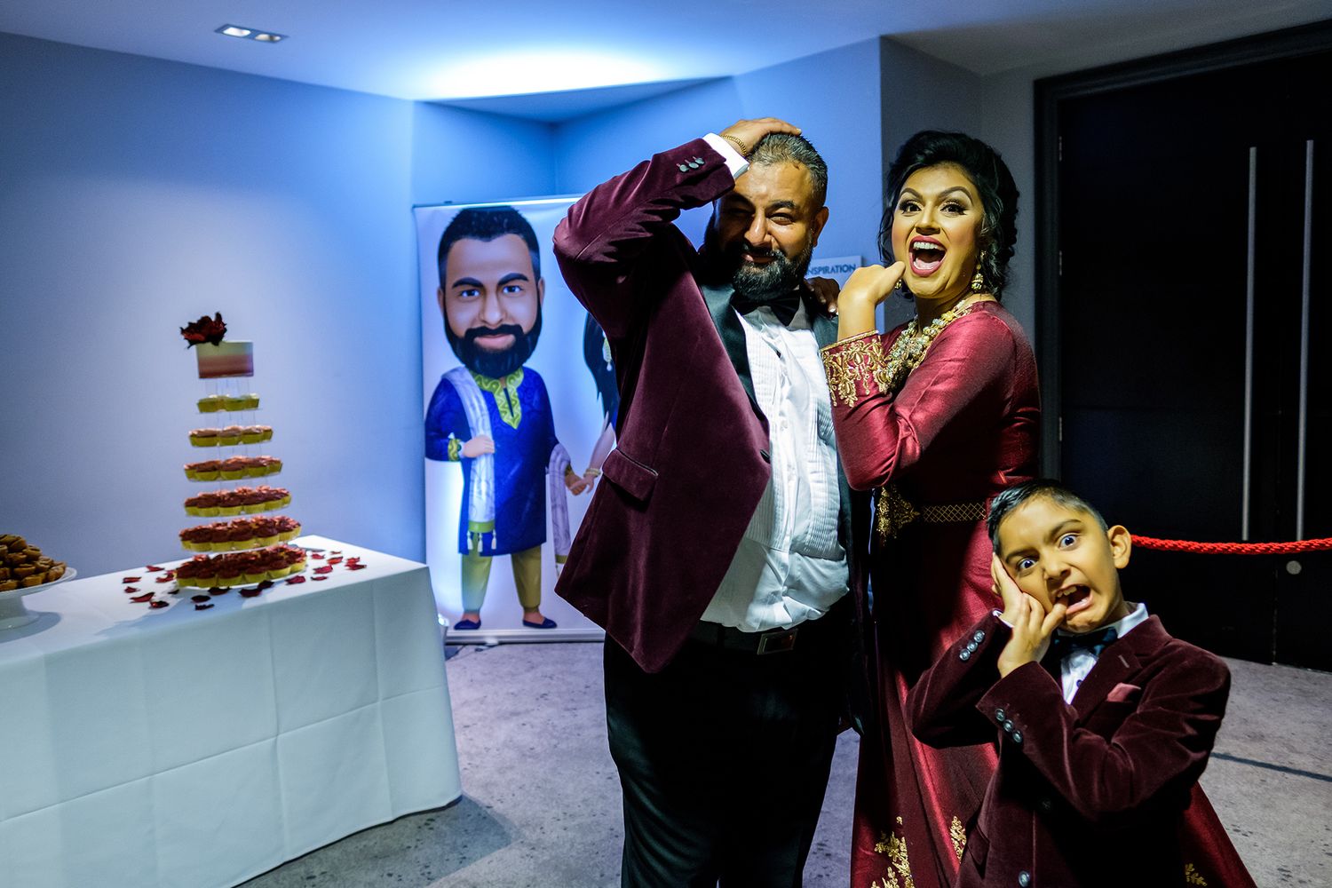 Fun reception moment with guests posing next to decorative cardboard cutouts in a blue-lit room.