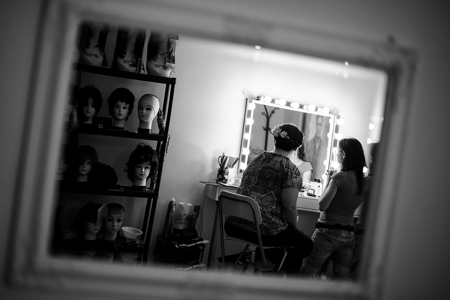 Black and white image of a dressing room with mirrors and wigs on display.