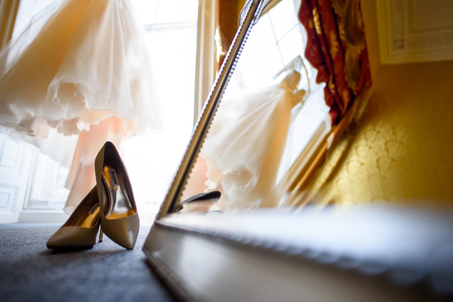 Elegant high heeled shoes rest on the floor next to dramatic window light and curtains.