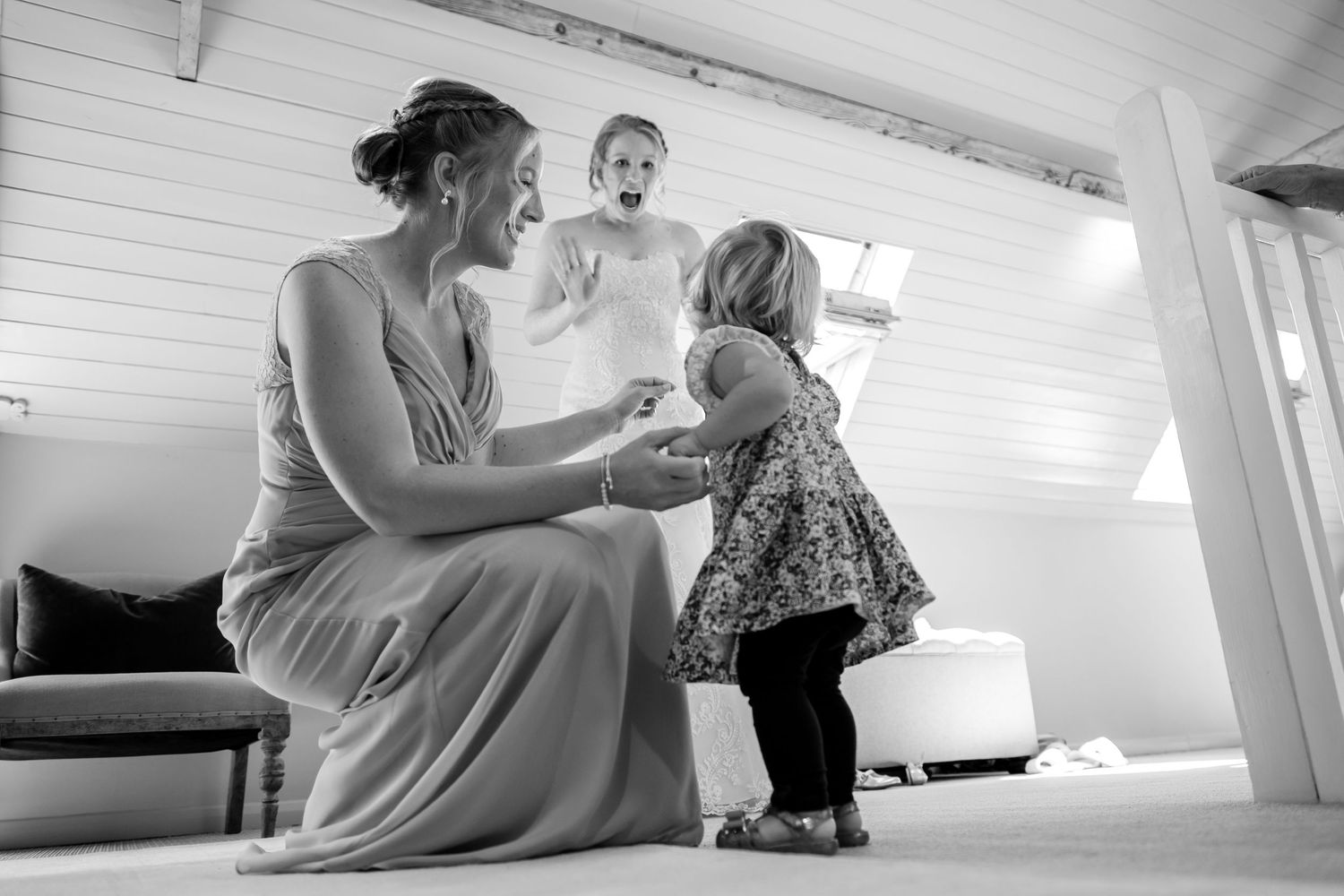 A group gathers in a white-walled attic room with exposed wooden beams during a celebration.