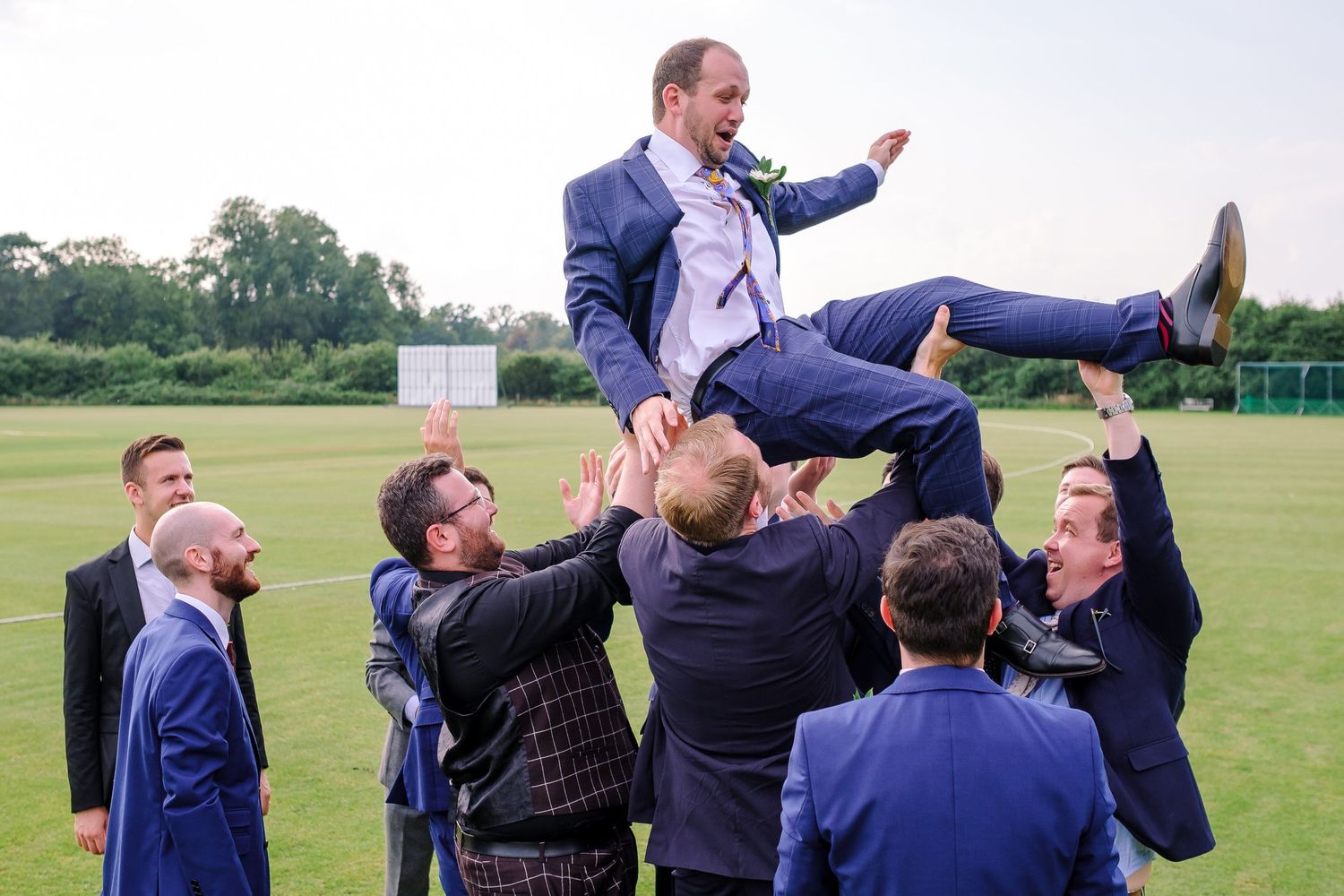 Groomsmen celebrate with joyful lifts and poses during outdoor wedding party photos.