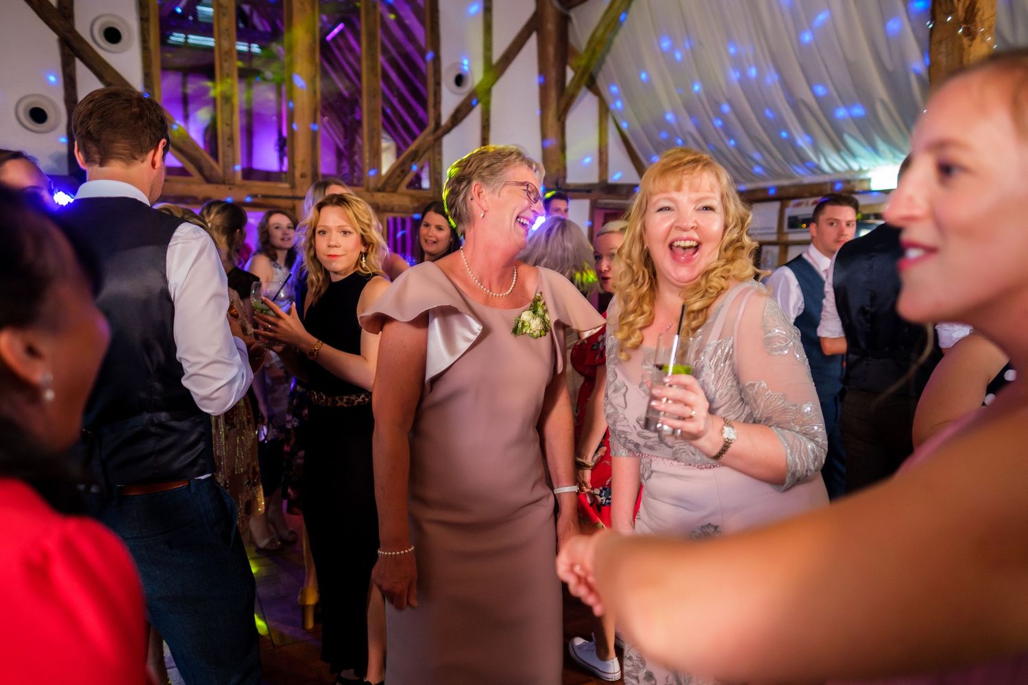 Wedding reception party with purple lighting and wooden beam decor.