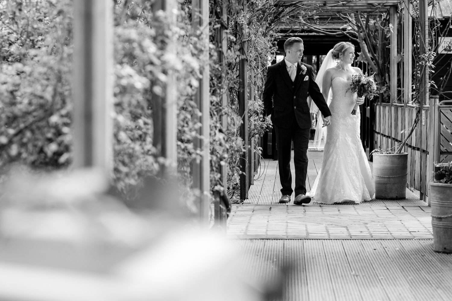 Black and white photo of a covered walkway with wedding guests walking through.